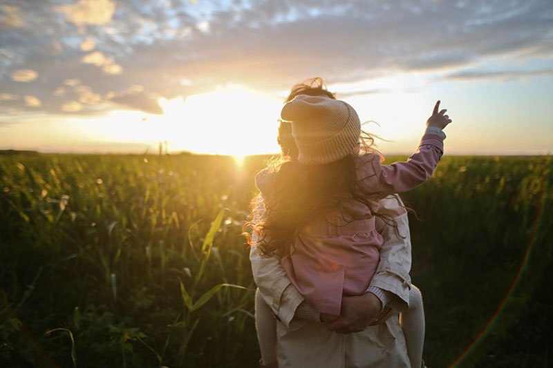 A woman holding a child in a field at sunset