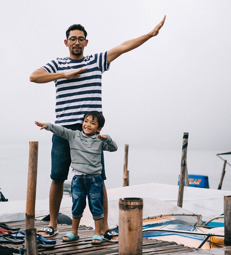 A father and son standing on a dock lifting arms in opposite directions